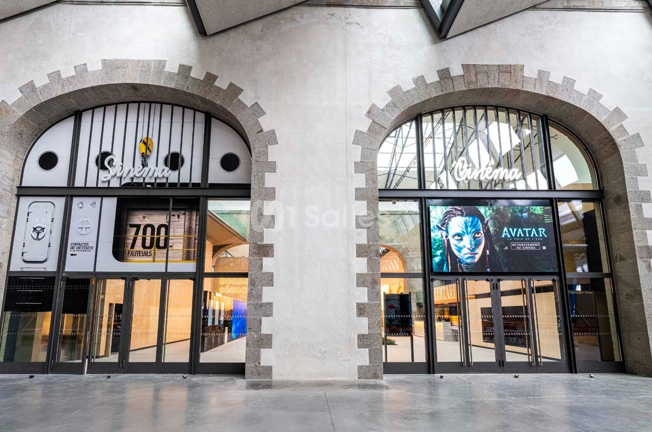 Façade d'un cinéma avec deux grandes portes vitrées, affiches de films et architecture en pierre apparente.