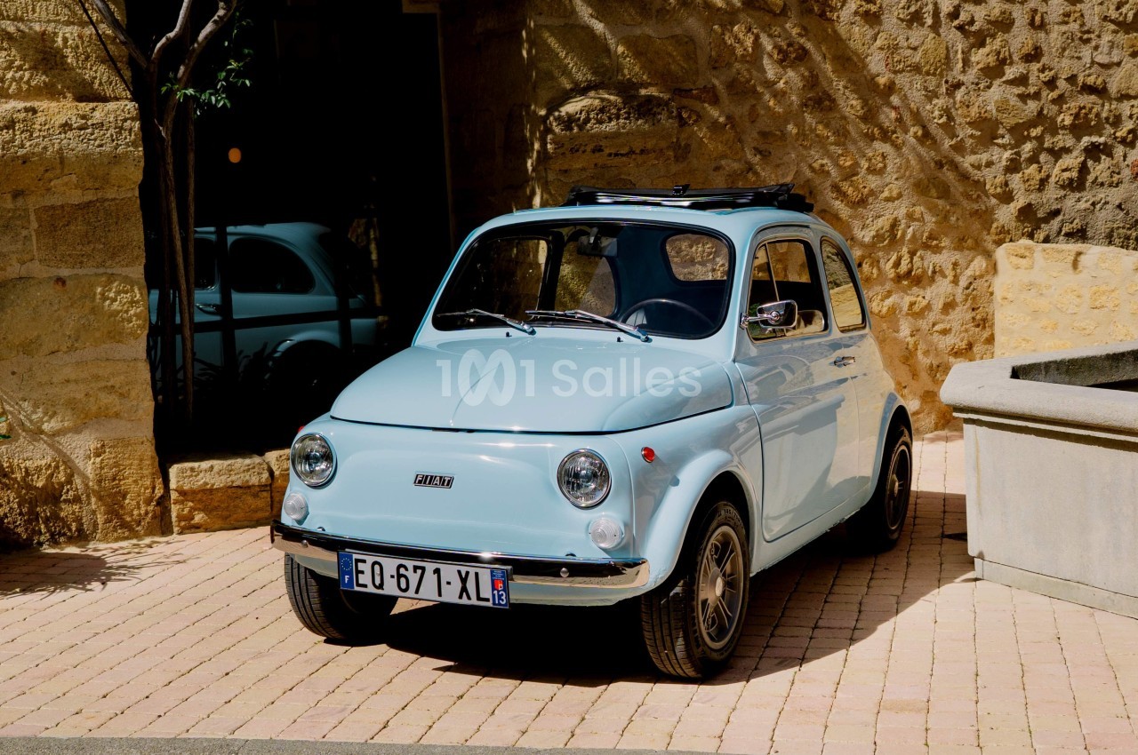 Voiture citadine vintage bleue garée sur un pavé devant un mur en pierre, toit ouvrant partiellement ouvert.