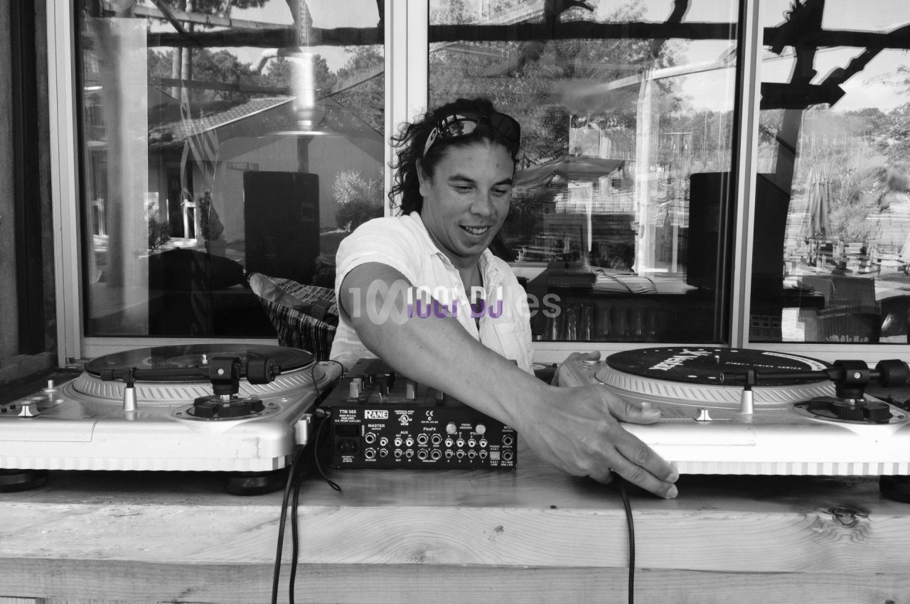 Un DJ mixant de la musique sur des platines vinyles, installé à l'extérieur devant une baie vitrée.