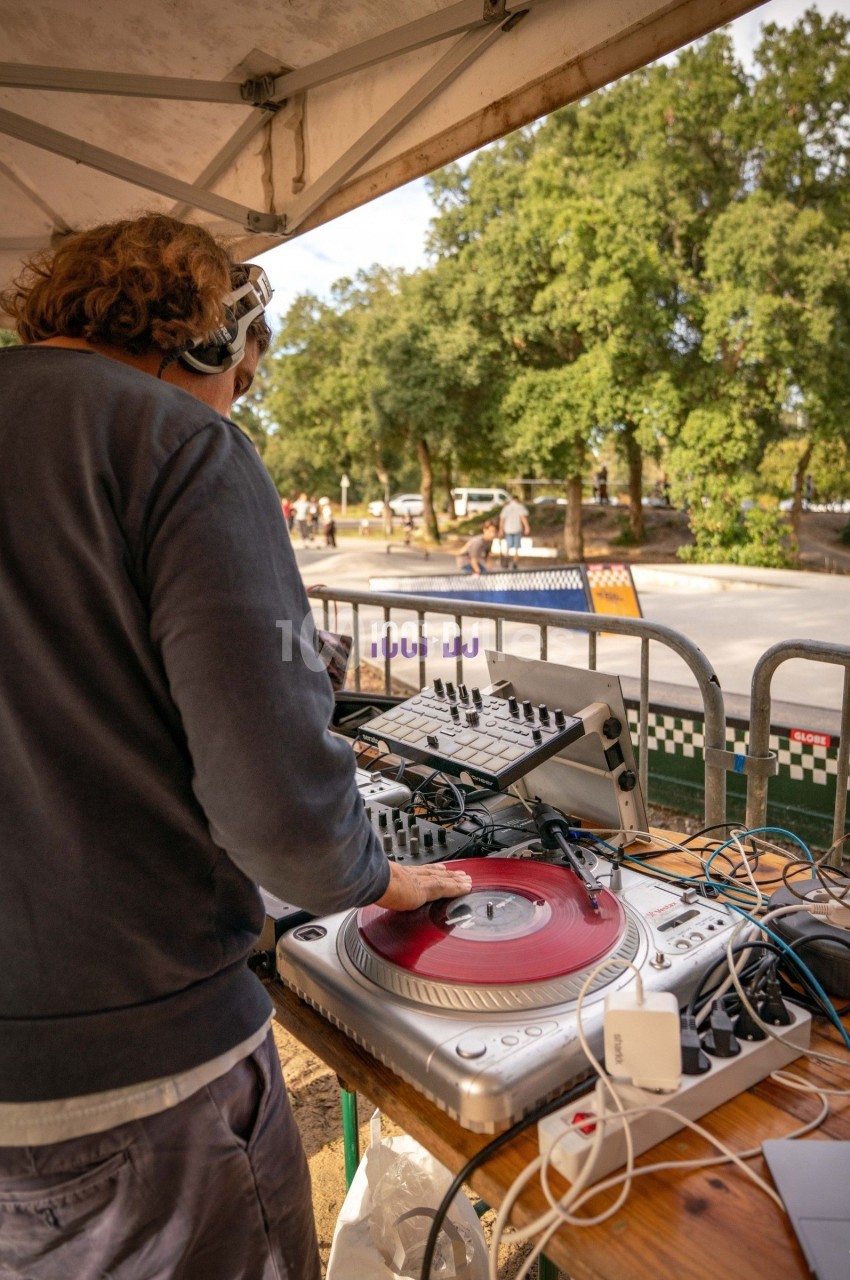 Un DJ mixe des vinyles sur une platine sous un chapiteau, avec un skatepark en arrière-plan.