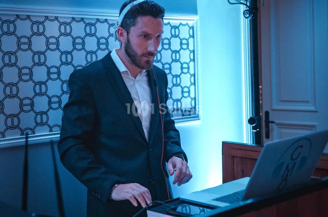 Un DJ en costume mixe de la musique sur un ordinateur portable dans un environnement éclairé en bleu.