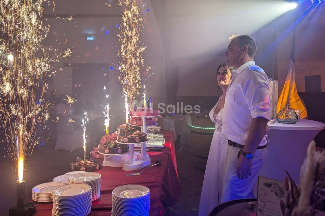 Un couple en tenue de mariage observe une table de desserts illuminée par des fontaines de feu dans une salle festive.