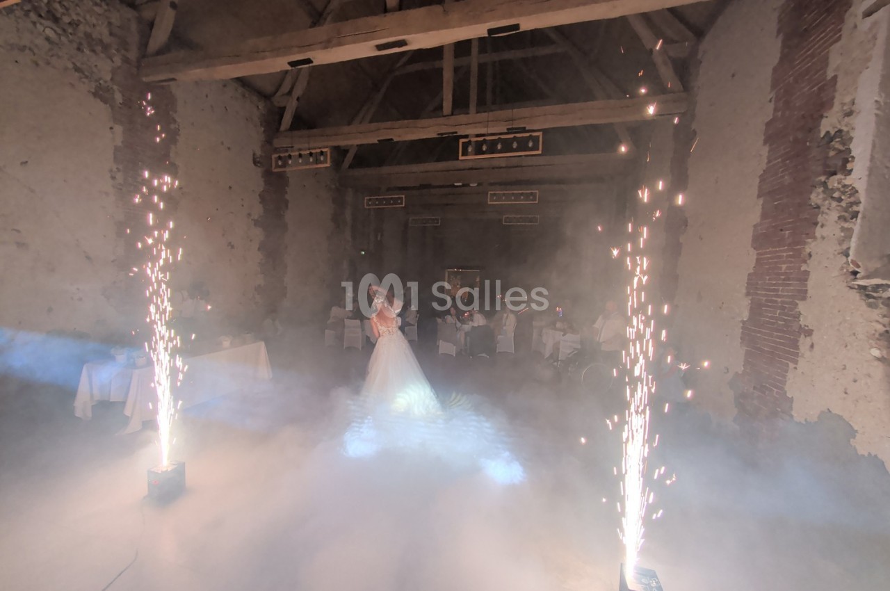 Mariée dans une salle en pierre avec effets de fumée et étincelles, entourée de tables dressées.