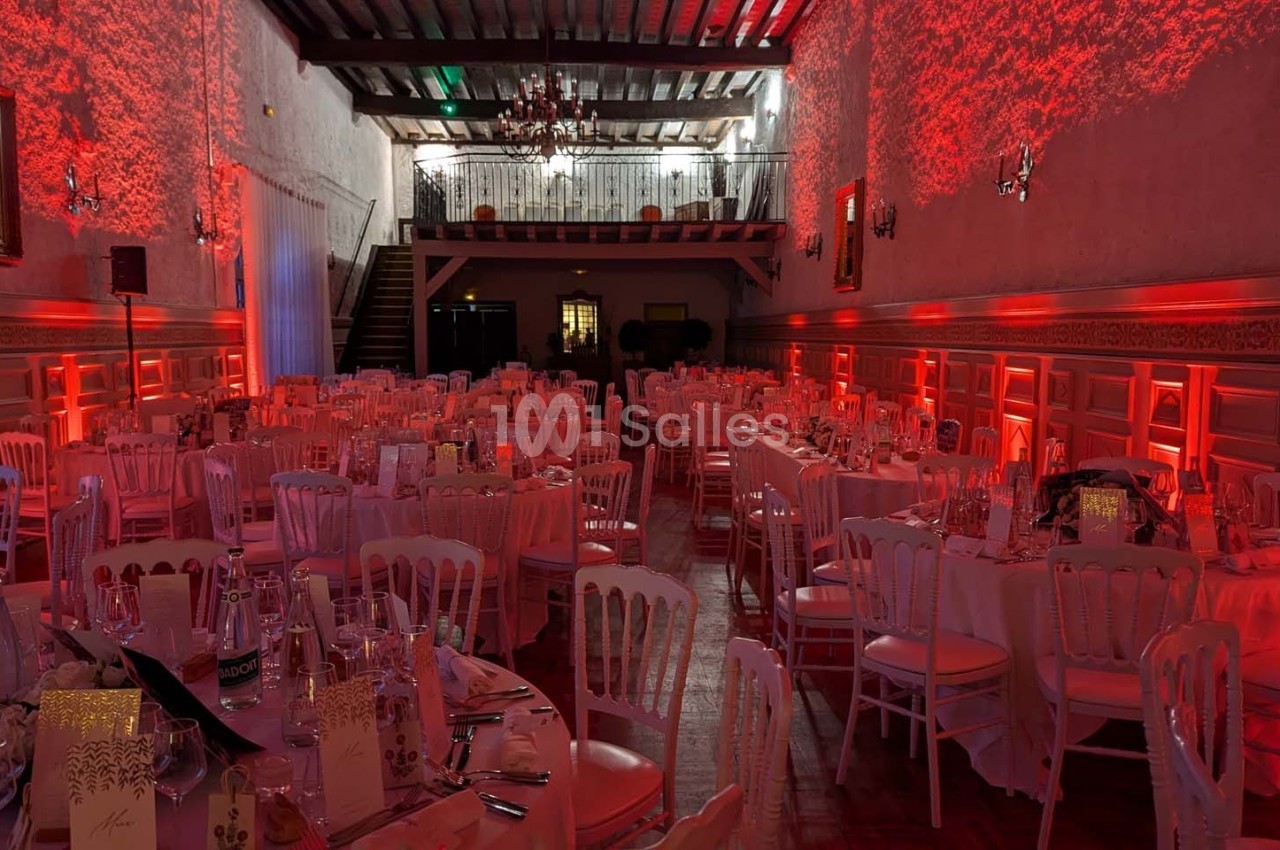 Salle de réception décorée avec des tables rondes, nappes blanches et éclairage rouge créant une ambiance chaleureuse.
