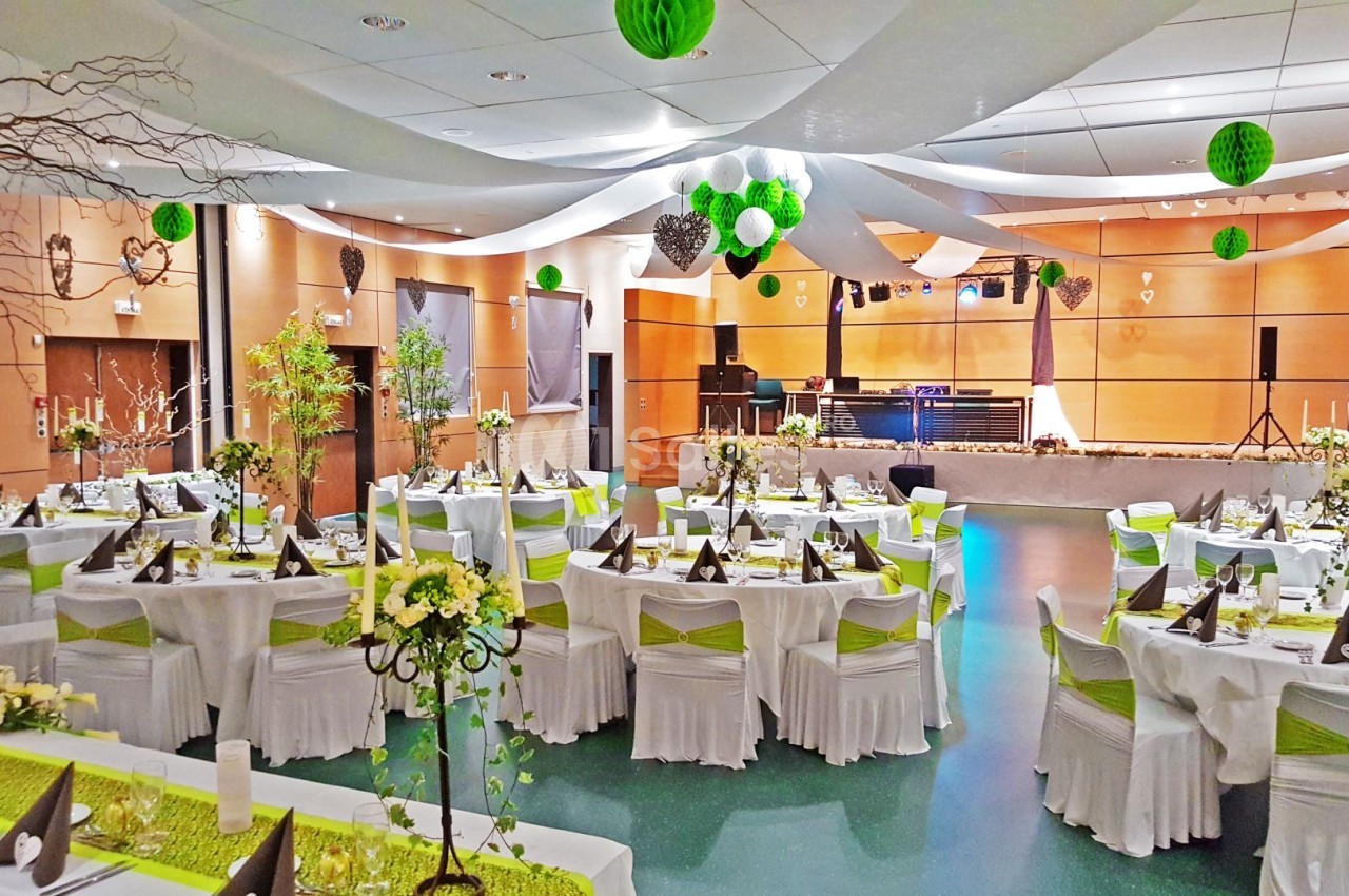 Salle de réception décorée avec des tables dressées, des chaises ornées de rubans verts et des suspensions en papier.