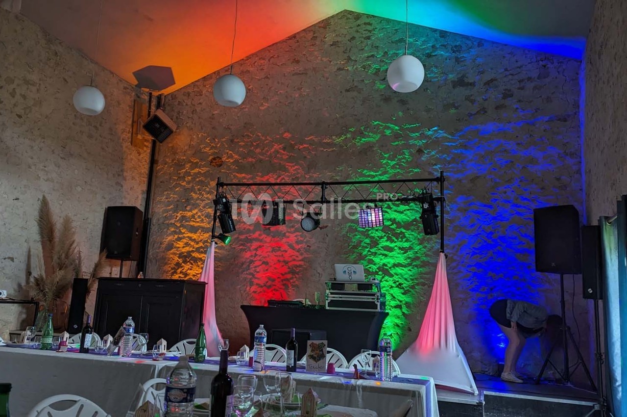 Salle décorée pour un événement avec éclairage coloré, tables dressées et équipement de sonorisation sur scène.