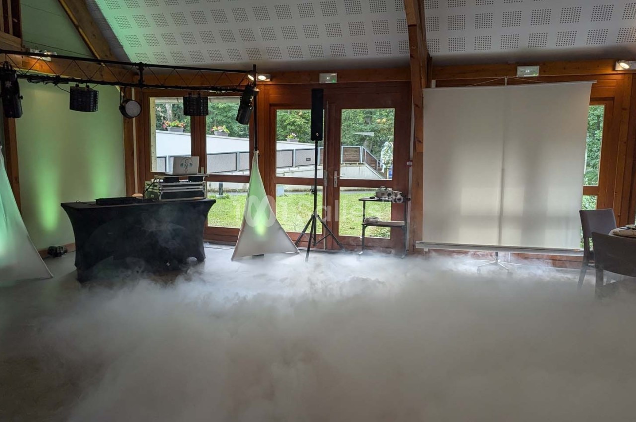 Salle de réception avec éclairage d'ambiance, fumée au sol et vue sur un espace extérieur verdoyant.