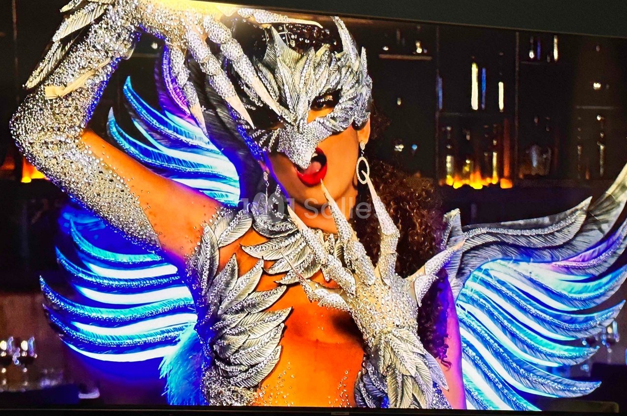 Personne portant un costume élaboré avec des ailes et un masque argenté, dans un décor intérieur faiblement éclairé.