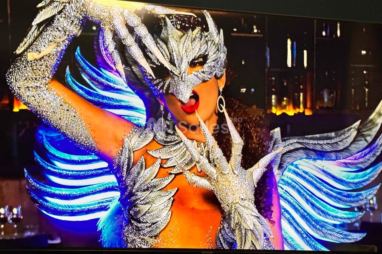 Personne portant un costume argenté étincelant avec des ailes et un masque élaboré, posant dans un décor sombre.