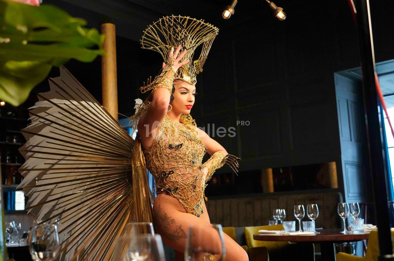 Personne en costume doré élaboré avec des éléments métalliques et une coiffe, posant dans un restaurant élégant.