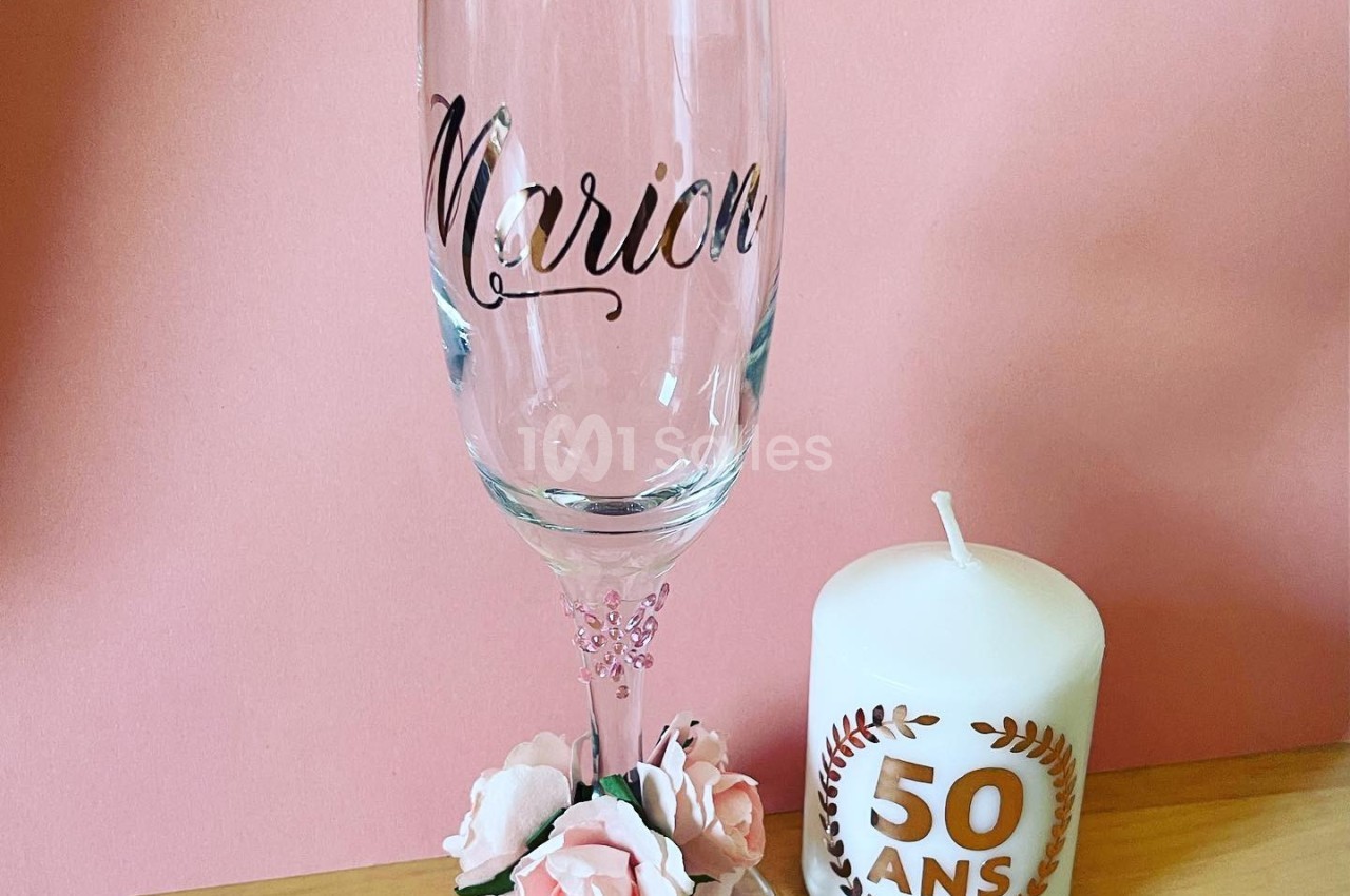 Flûte à champagne personnalisée avec des roses décoratives et une bougie blanche marquée ’50 ans’ sur une table en bois.