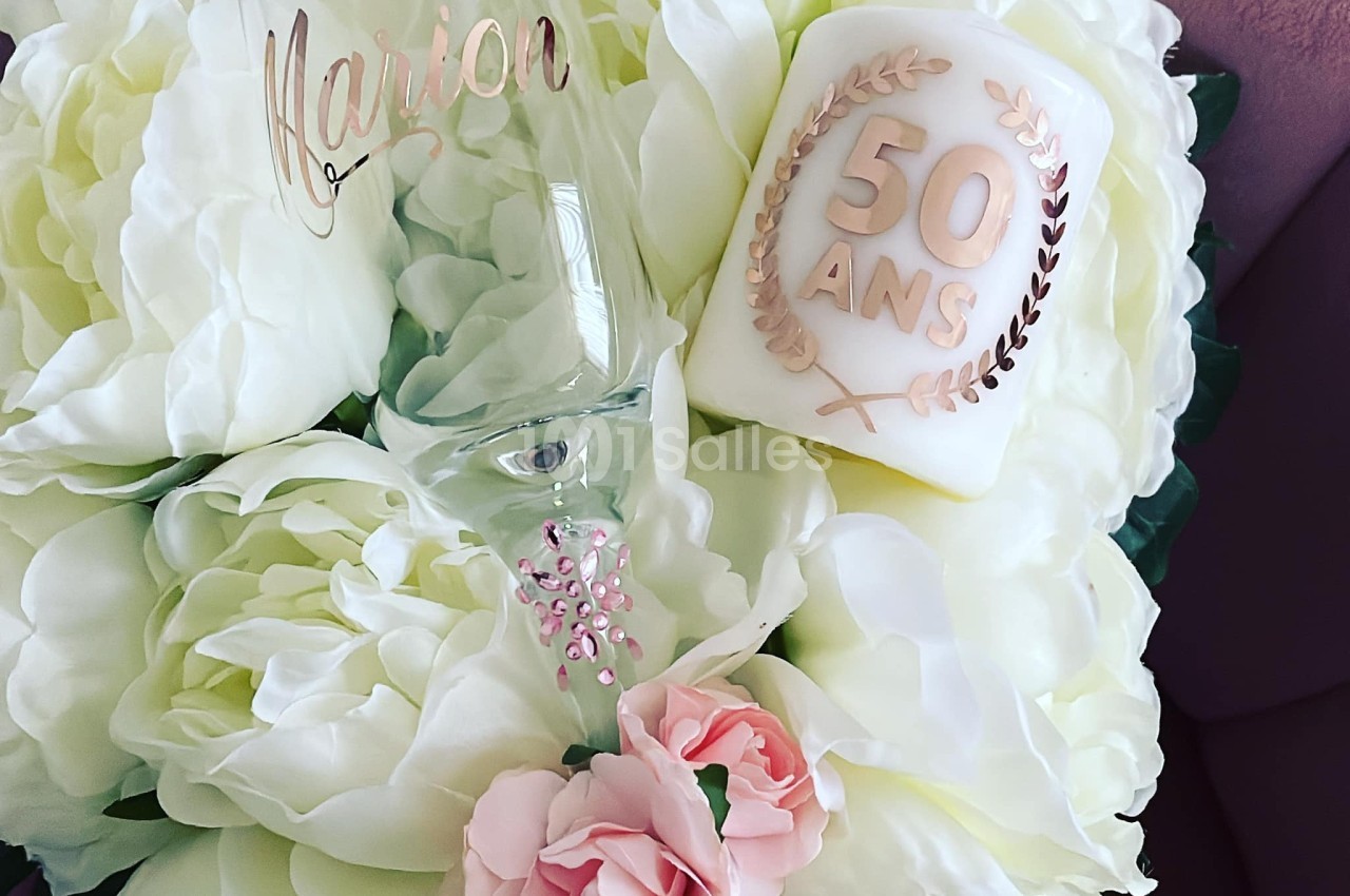 Bouquet de fleurs blanches et roses avec une flûte gravée et une bougie marquée ’50 ans’.