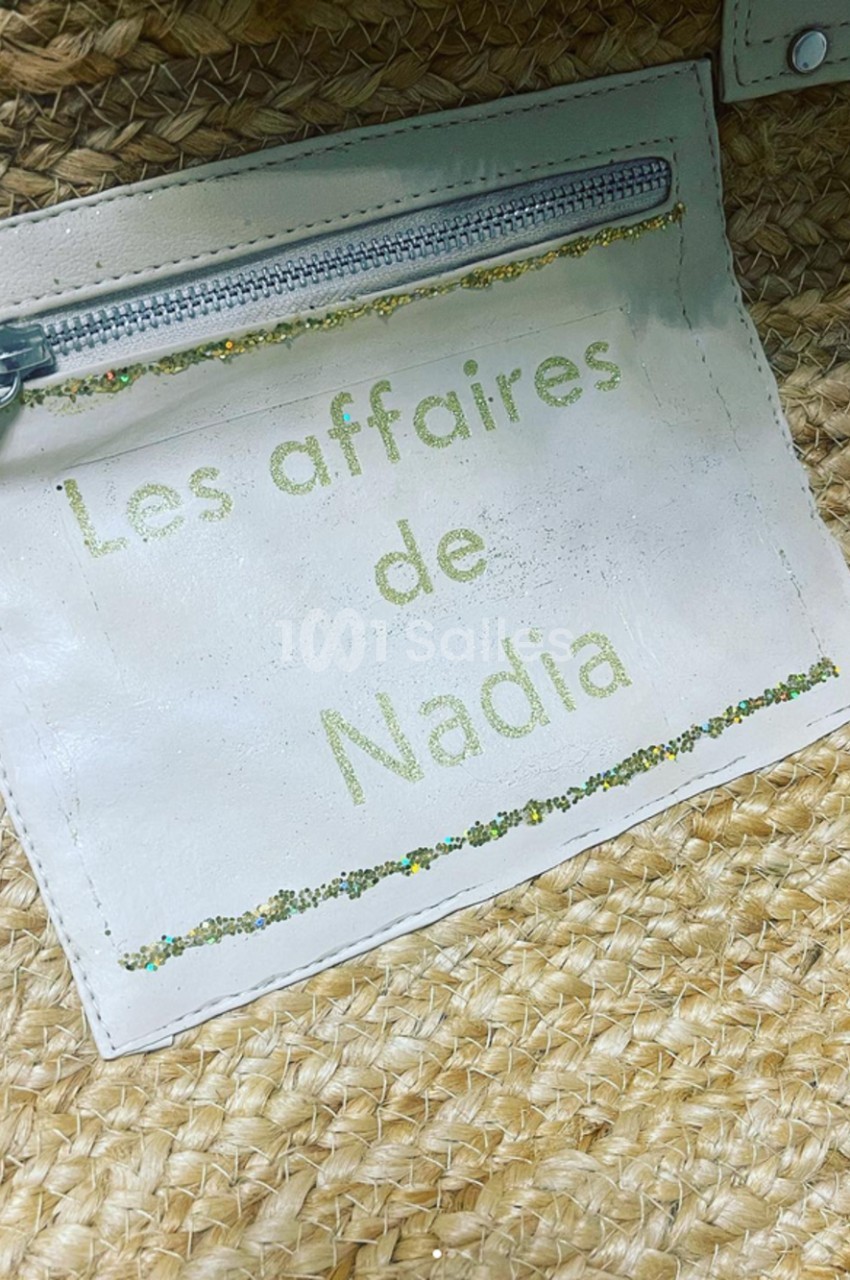 Étiquette en cuir blanc avec une fermeture éclair, portant l'inscription ’Les affaires de Nadia’, sur un sac en paille…