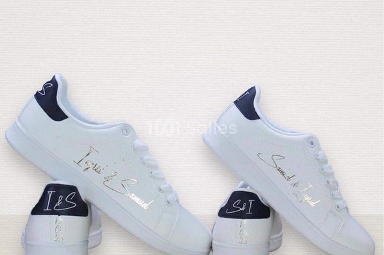 Chaussures blanches avec détails personnalisés en écriture argentée et talons bleu marine, posées sur une surface claire.