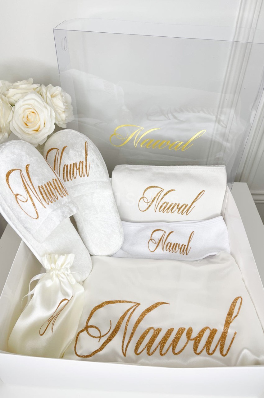 Coffret contenant des articles personnalisés avec le prénom ’Nawal’ : serviettes, chaussons, pochette et boîte transparente.