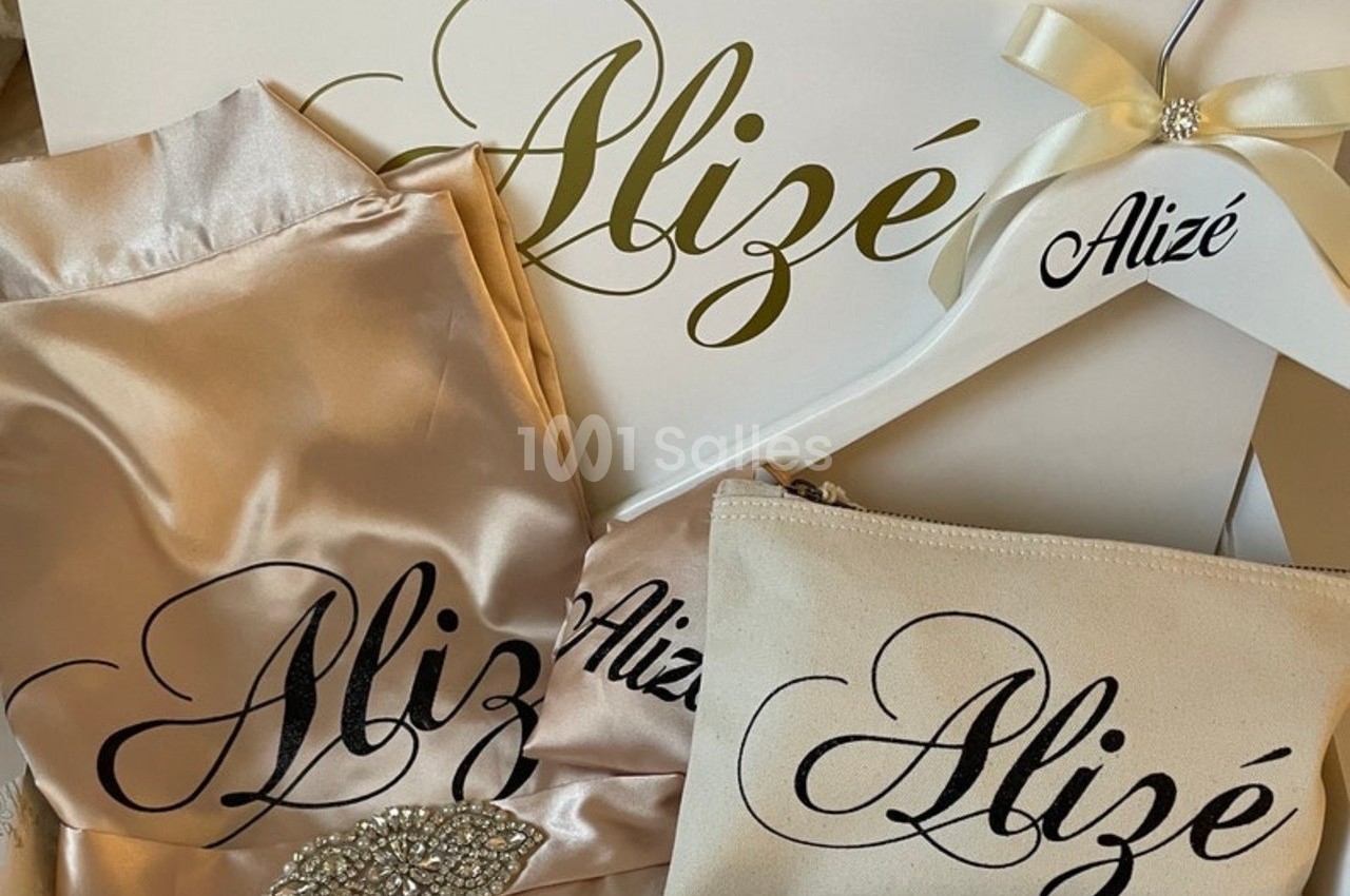 Ensemble d'articles personnalisés en satin beige, comprenant un cintre, une pochette et un tissu, avec le nom ’Alizé’.