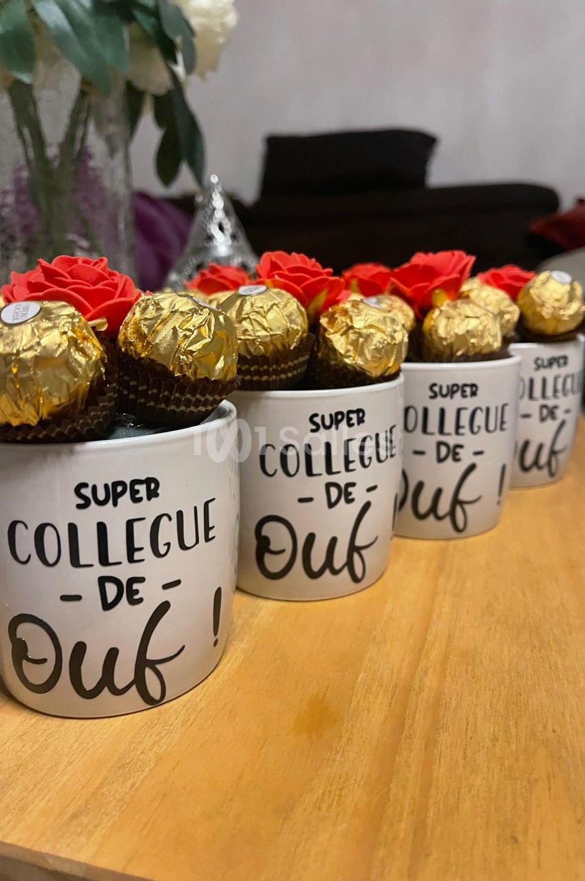 Tasses blanches avec l'inscription ’Super collègue de ouf !’ remplies de chocolats dorés et décorées de fleurs rouges.