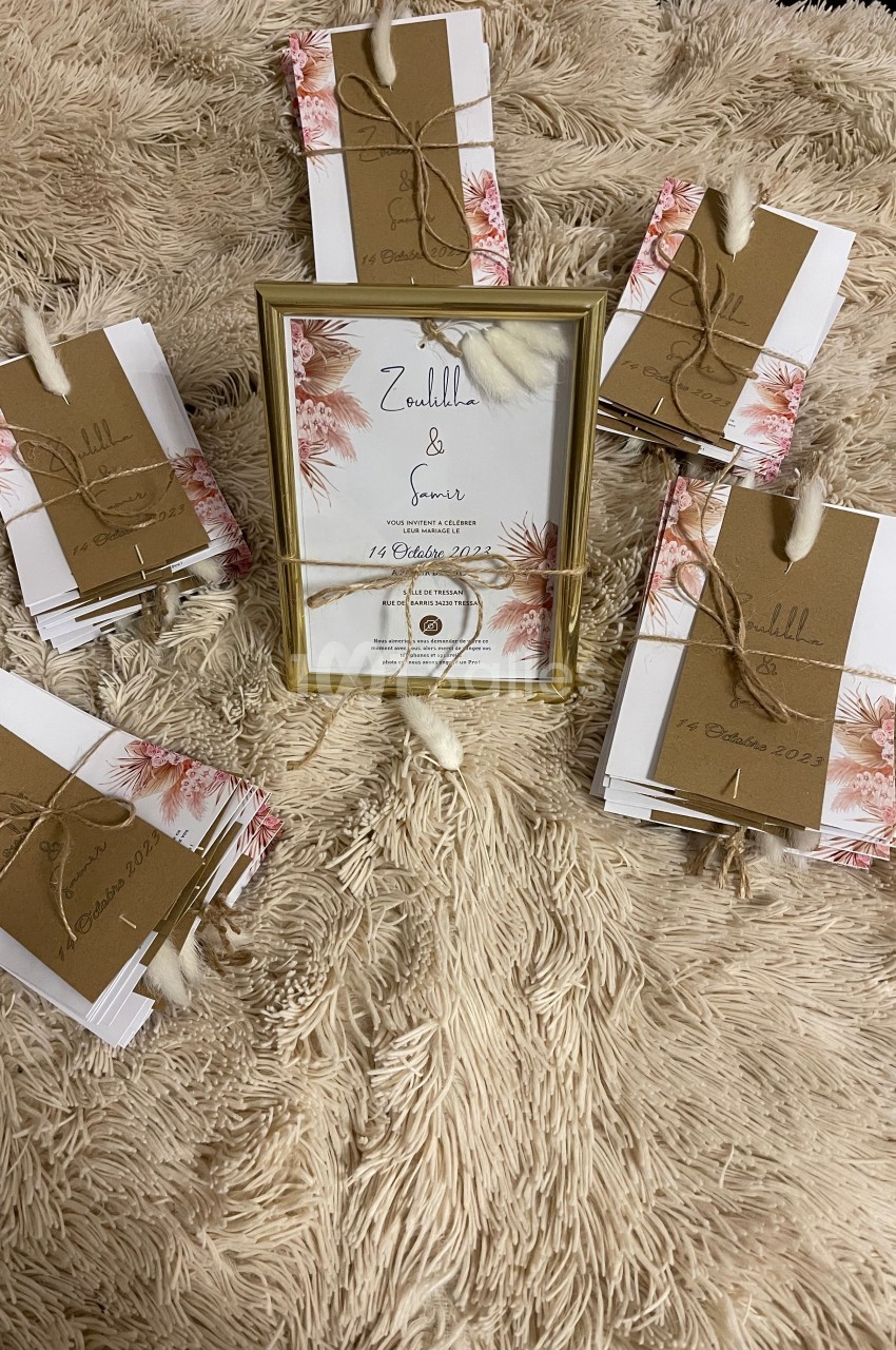 Cartes d'invitation décorées avec des fleurs et des enveloppes kraft, disposées autour d'un cadre doré sur un tapis beige.