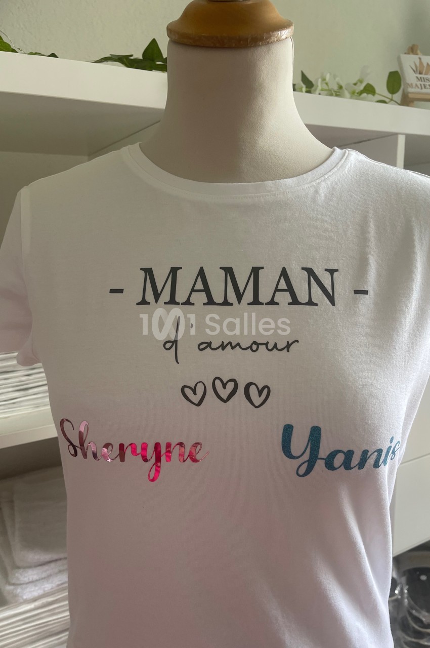 T-shirt blanc avec l'inscription ’MAMAN d'amour’ et les prénoms ’Sheryne’ et ’Yanis’ imprimés en couleurs.