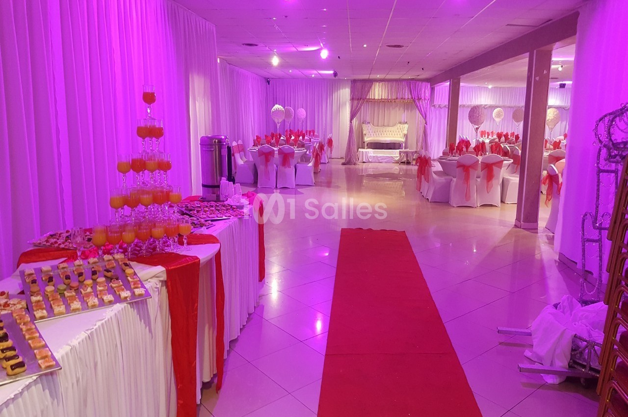 Salle de réception décorée en blanc et rouge avec tables dressées, buffet de desserts et éclairage violet.