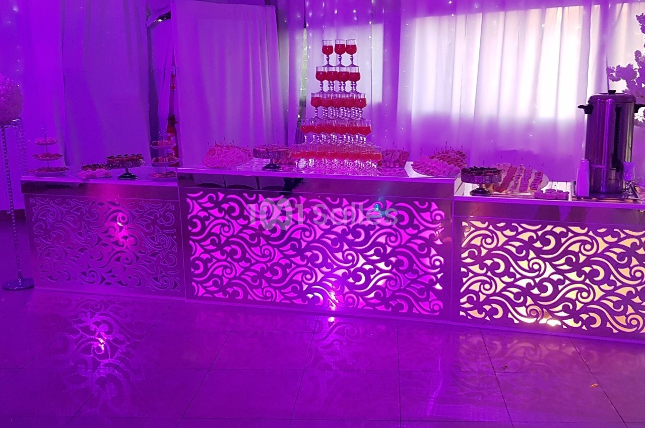 Buffet décoratif éclairé en violet avec des desserts variés et une fontaine à boissons en arrière-plan.
