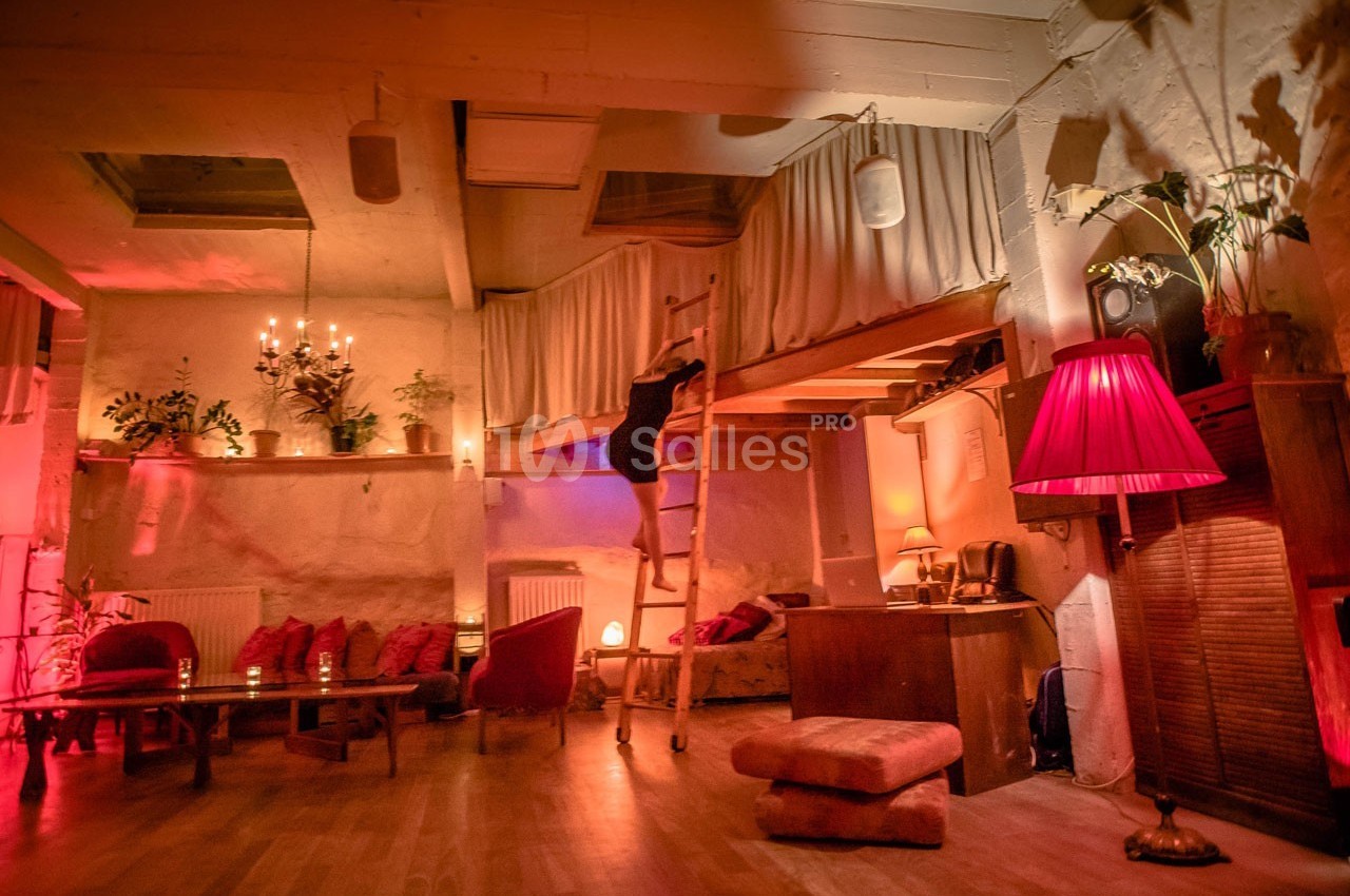 Intérieur chaleureux avec éclairage tamisé, canapé, plantes et mezzanine accessible par une échelle en bois.