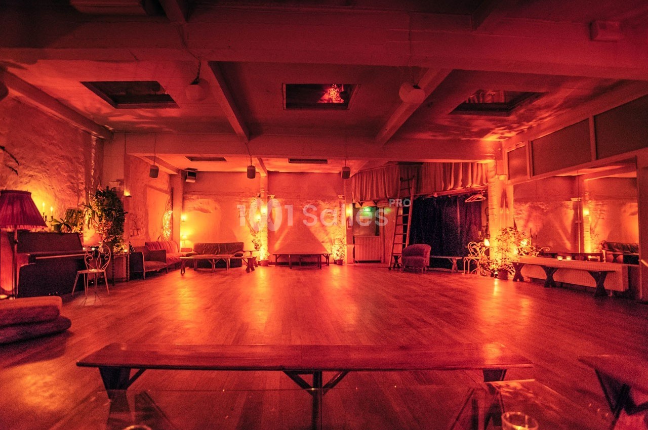 Salle spacieuse à l'éclairage tamisé rouge-orange, avec bancs, plantes et ambiance chaleureuse.
