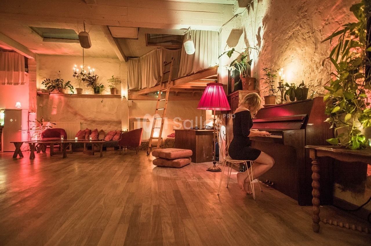 Une femme joue du piano dans une pièce chaleureuse avec éclairage tamisé, plantes et mobilier en bois.
