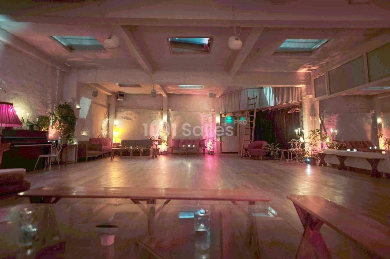 Salle spacieuse avec parquet, éclairage tamisé coloré, canapés et plantes disposés le long des murs.