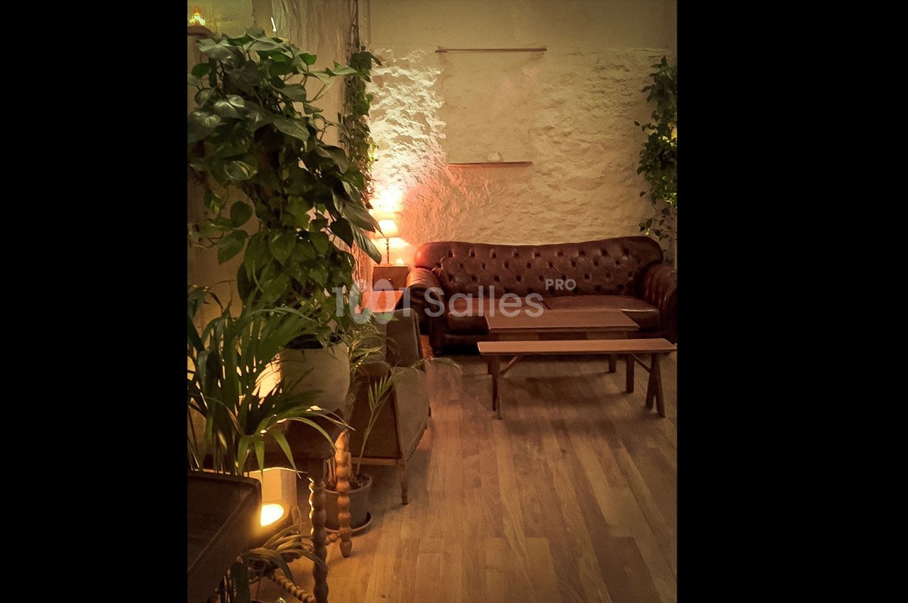 Salon cosy avec canapé en cuir, tables basses en bois, plantes vertes et éclairage tamisé.