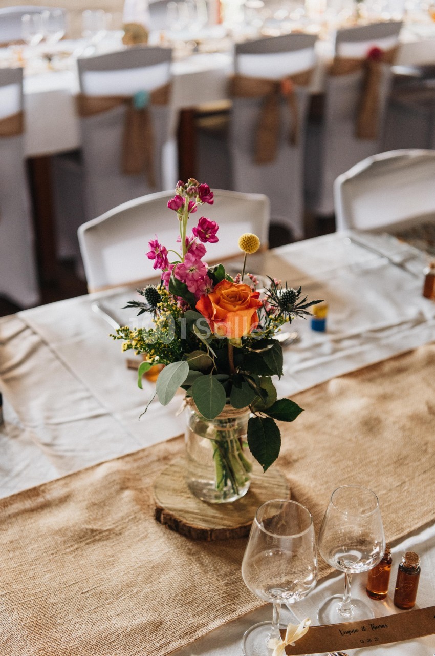 Centre de table avec un bouquet de fleurs colorées dans un vase en verre, posé sur une nappe en toile de jute.