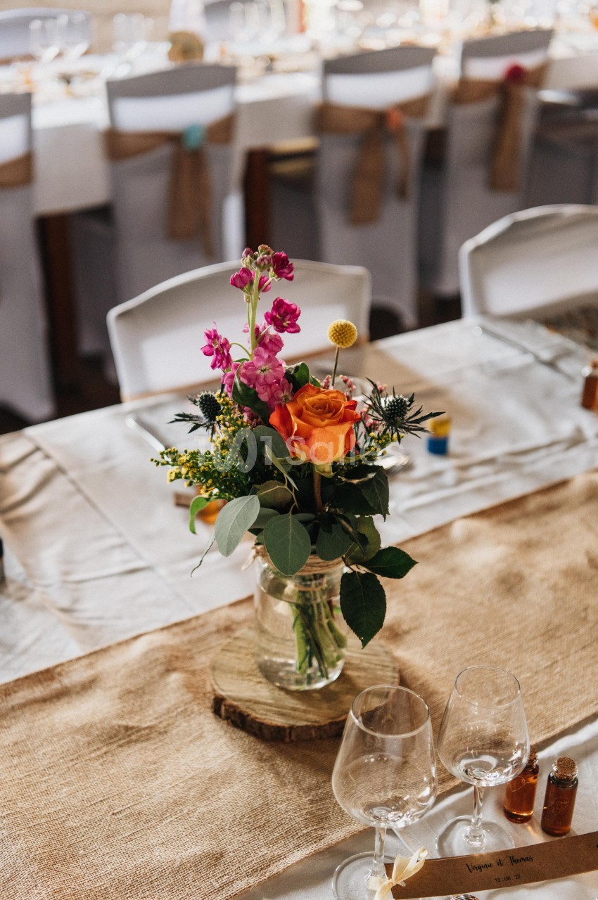 Centre de table avec un bouquet de fleurs colorées dans un vase en verre, posé sur une nappe en toile de jute.