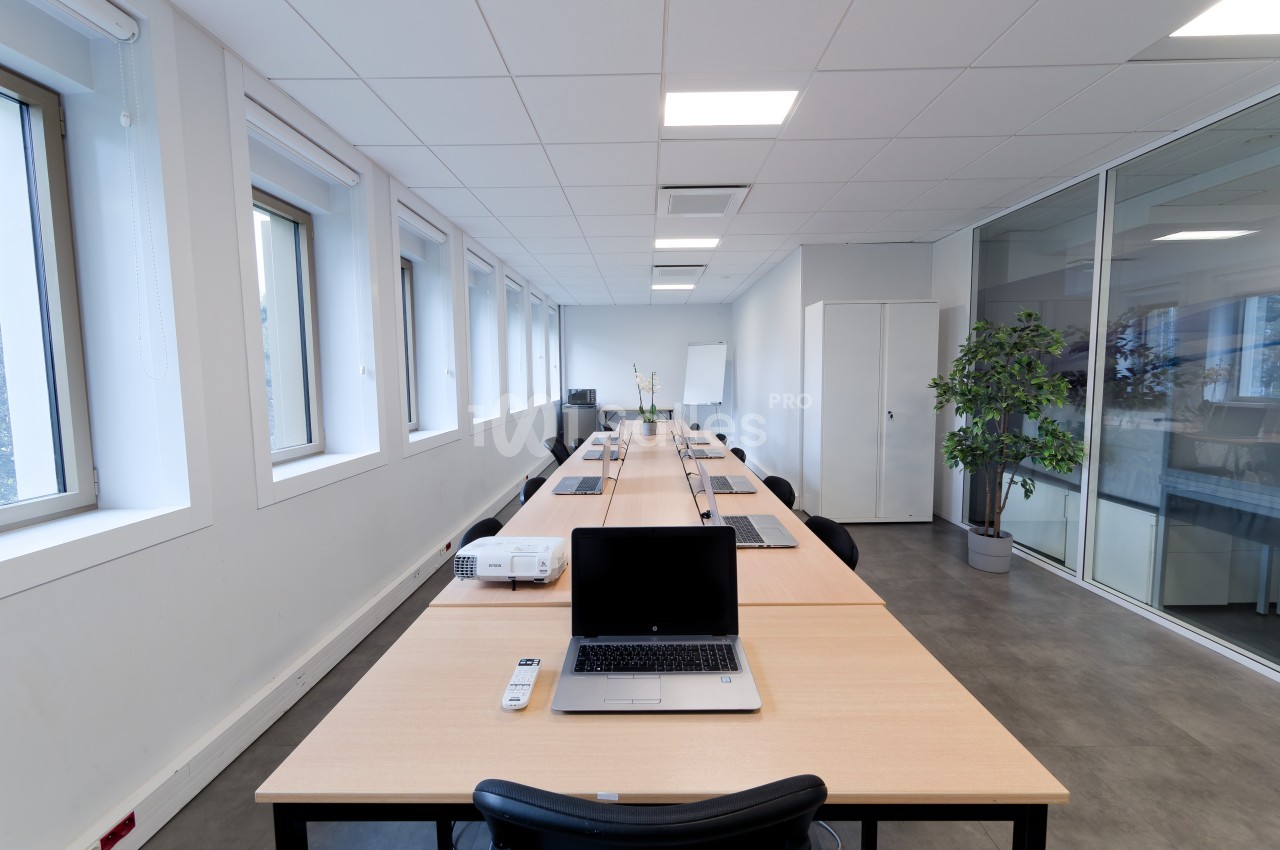 Salle de réunion lumineuse avec une grande table, des ordinateurs portables, un projecteur et des chaises.