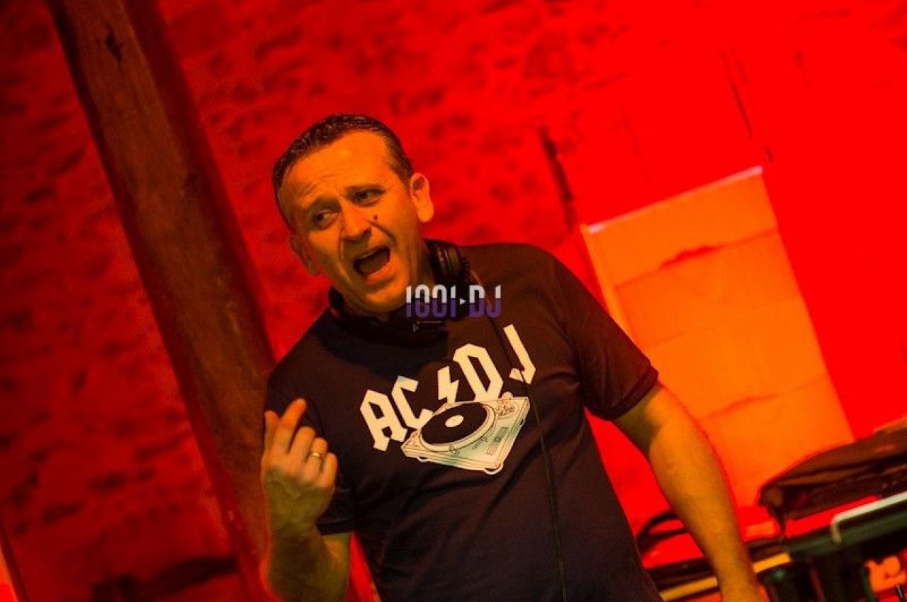 Un DJ mixant sur une table de mixage dans une ambiance lumineuse rouge, dans un espace en briques apparentes.