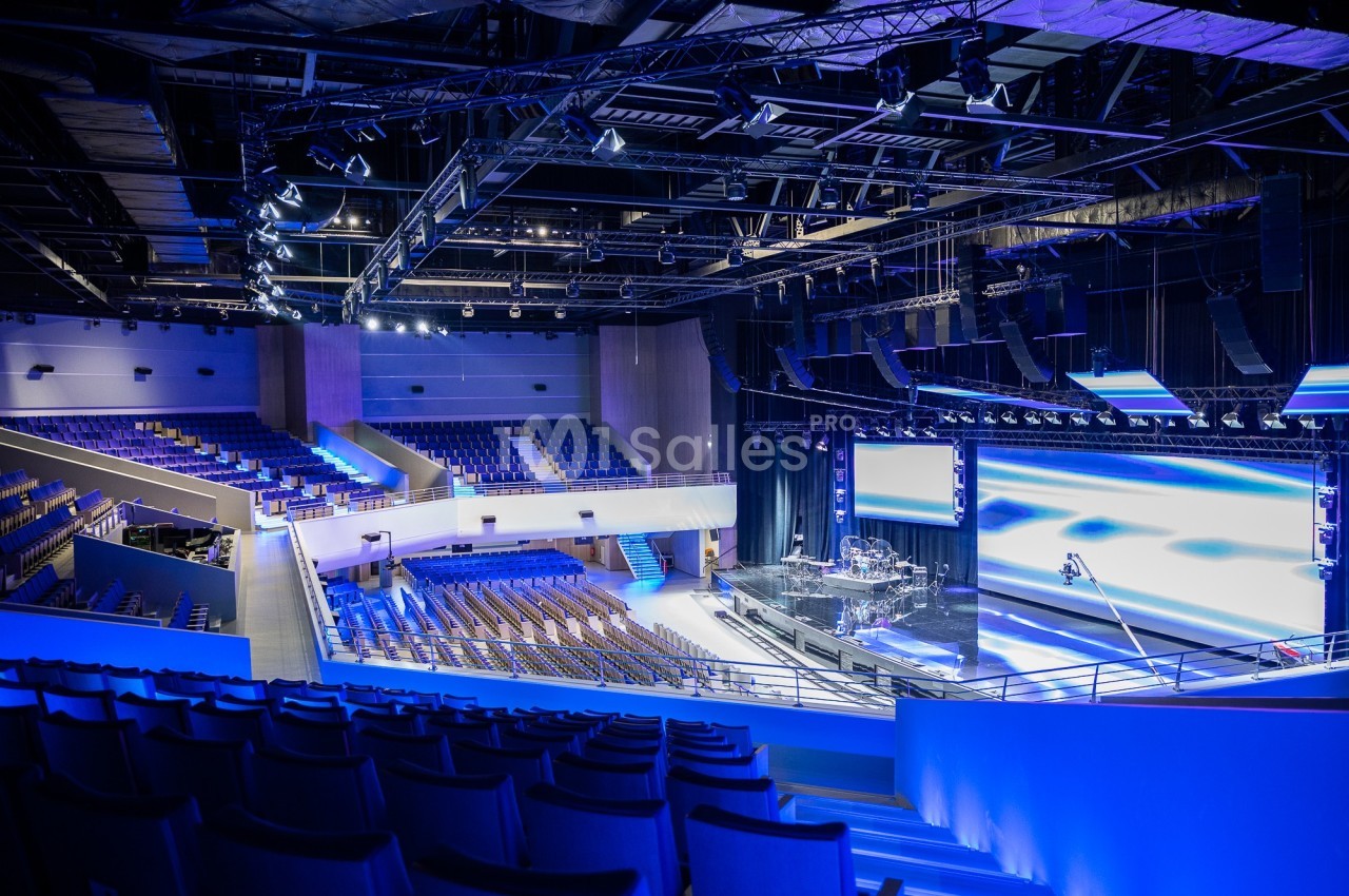 Salle de spectacle moderne avec scène équipée, éclairage professionnel et rangées de sièges vides en gradins.