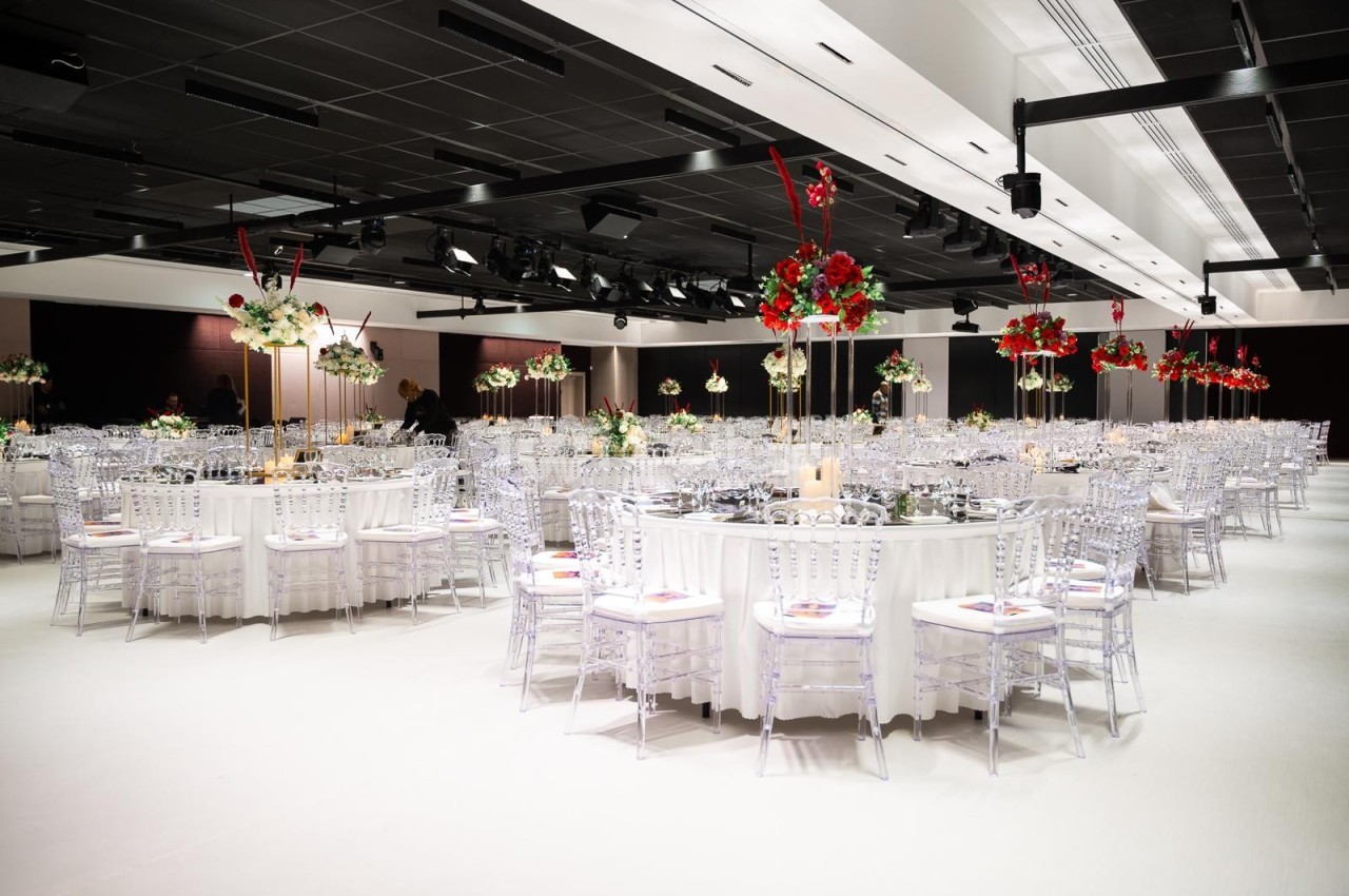 Salle de réception élégante avec tables rondes décorées de nappes blanches, fleurs rouges et blanches, et chaises…