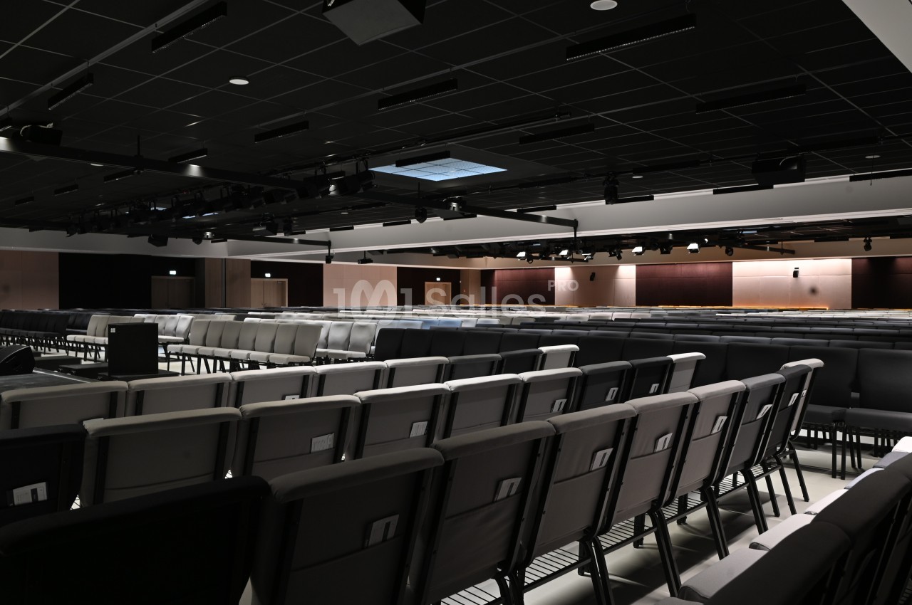 Salle de conférence vide avec rangées de sièges alignés et plafond équipé de luminaires.
