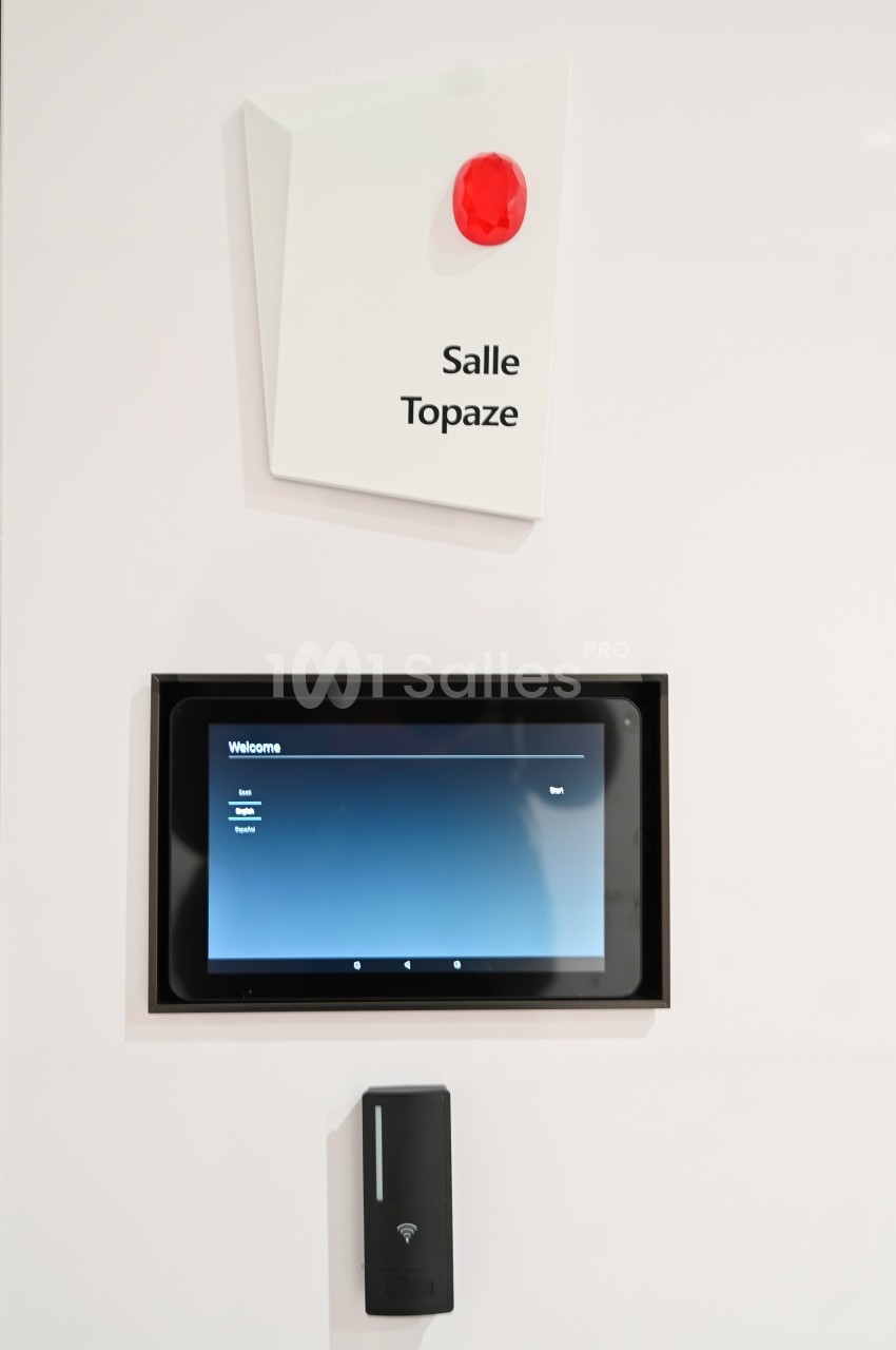 Panneau indiquant ’Salle Topaze’ avec une tablette tactile et un lecteur de badge en dessous.