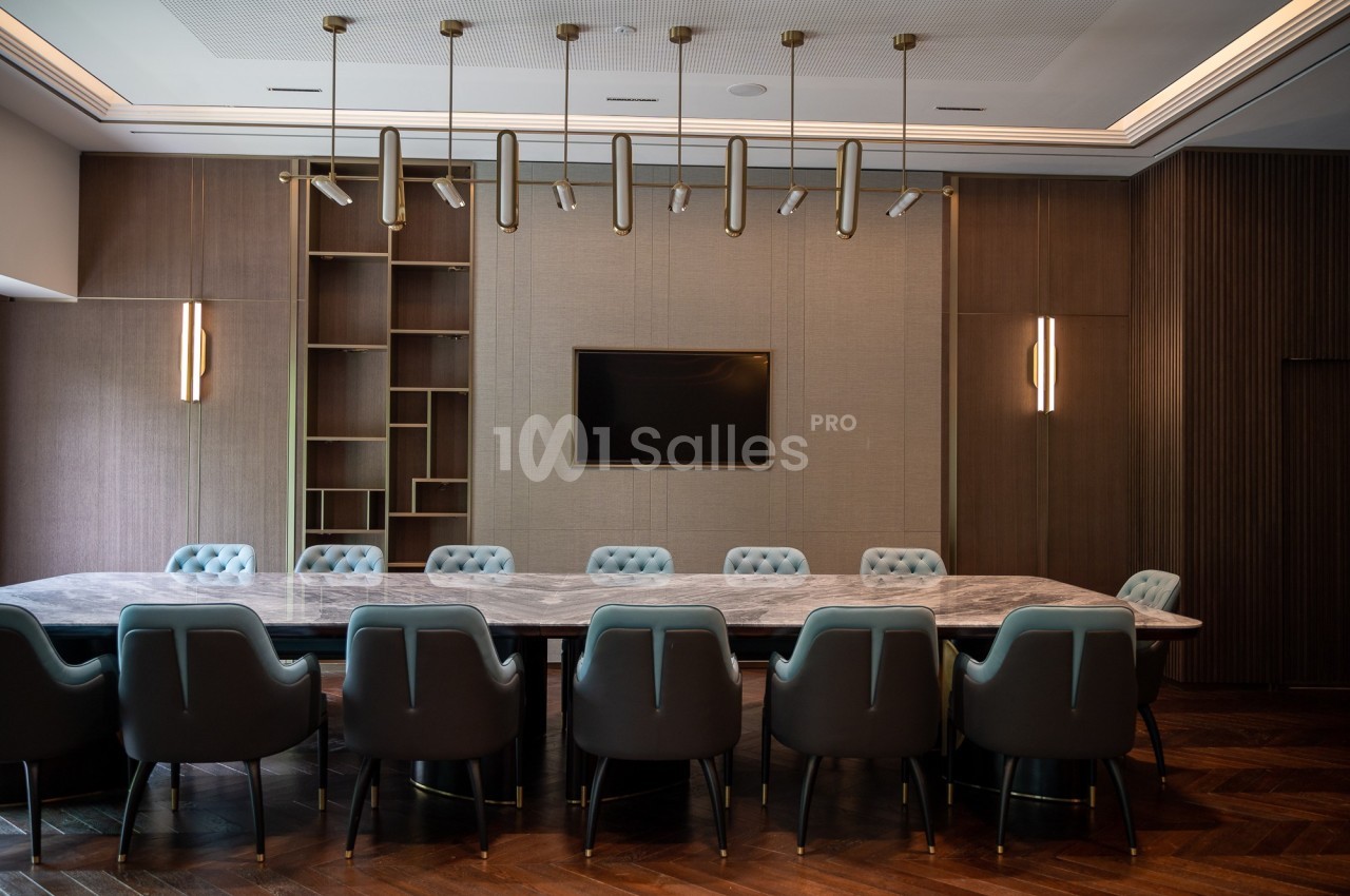 Salle de réunion moderne avec une grande table en marbre, des chaises rembourrées et un écran mural.