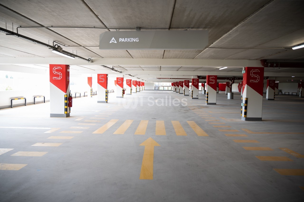 Parking couvert vide avec marquages au sol jaunes et panneaux rouges indiquant les emplacements.