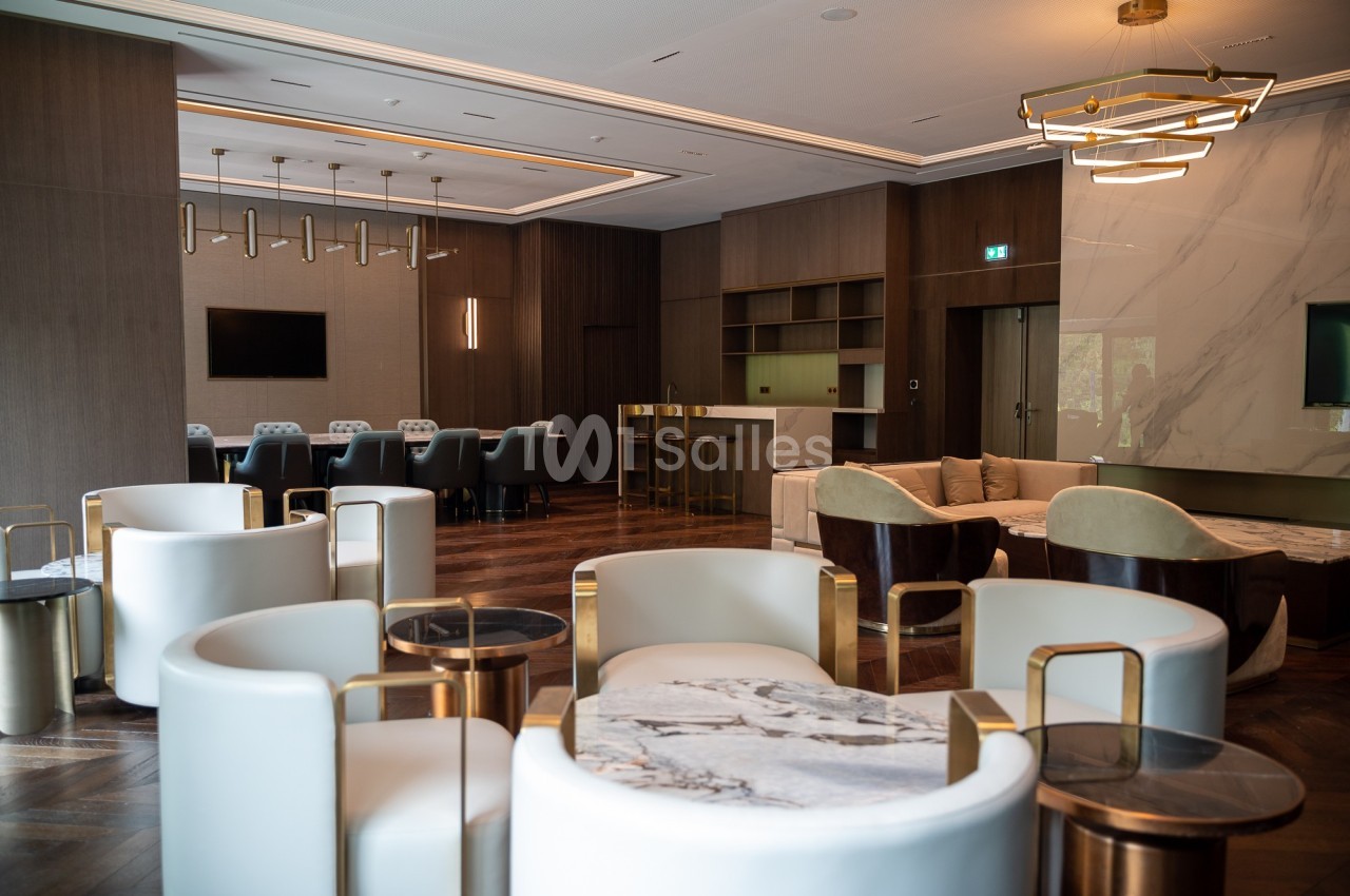 Salle moderne avec mobilier élégant, fauteuils blancs, tables en marbre, parquet en bois et éclairage design.