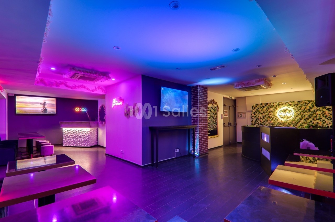 Salle moderne avec éclairage coloré, tables et comptoir, décorations murales et écran lumineux.