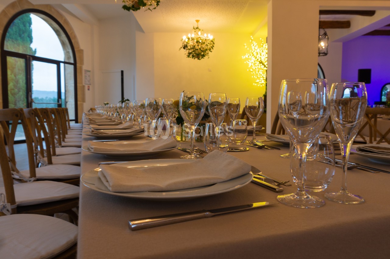 Salle de réception élégamment décorée avec une longue table dressée, des assiettes, verres et serviettes.