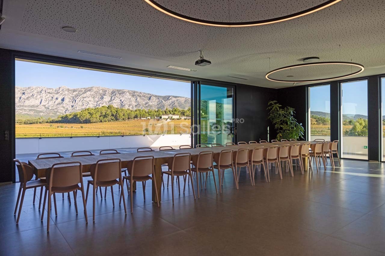 Salle de réunion lumineuse avec une grande table, vue sur un paysage de montagne et des baies vitrées ouvertes.