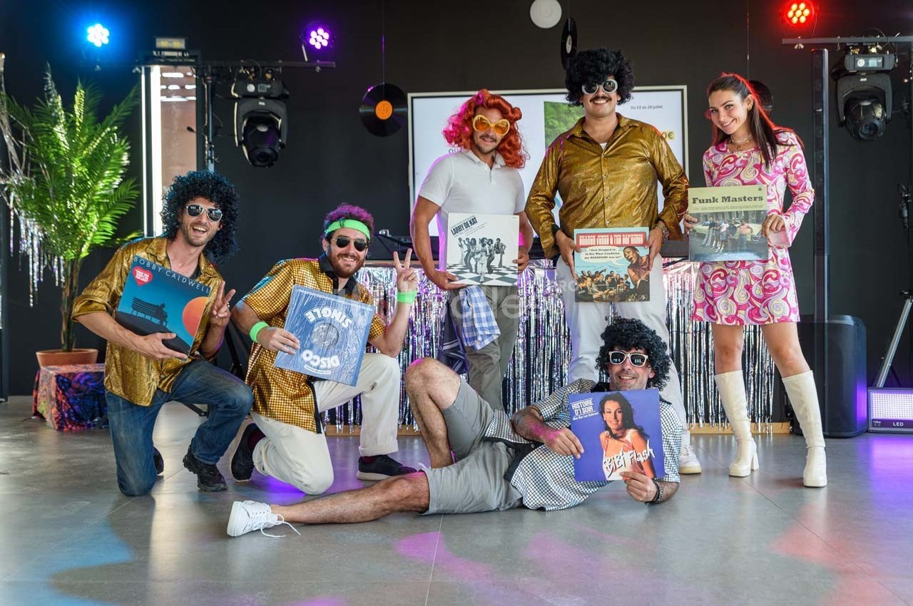 Un groupe de personnes en tenues rétro posant avec des disques vinyles dans un décor festif et coloré.