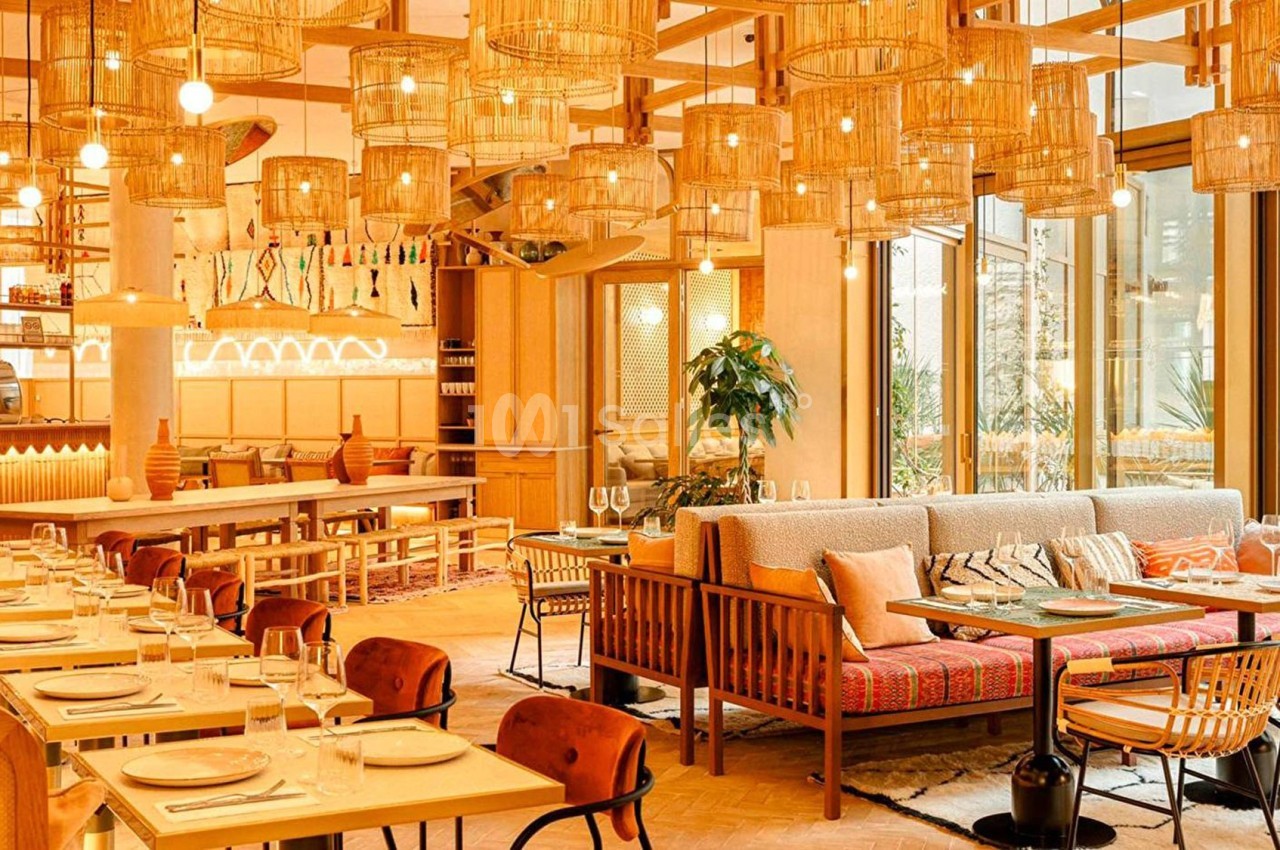 Salle de restaurant lumineuse avec mobilier en bois, lampes suspendues en osier et tables dressées.
