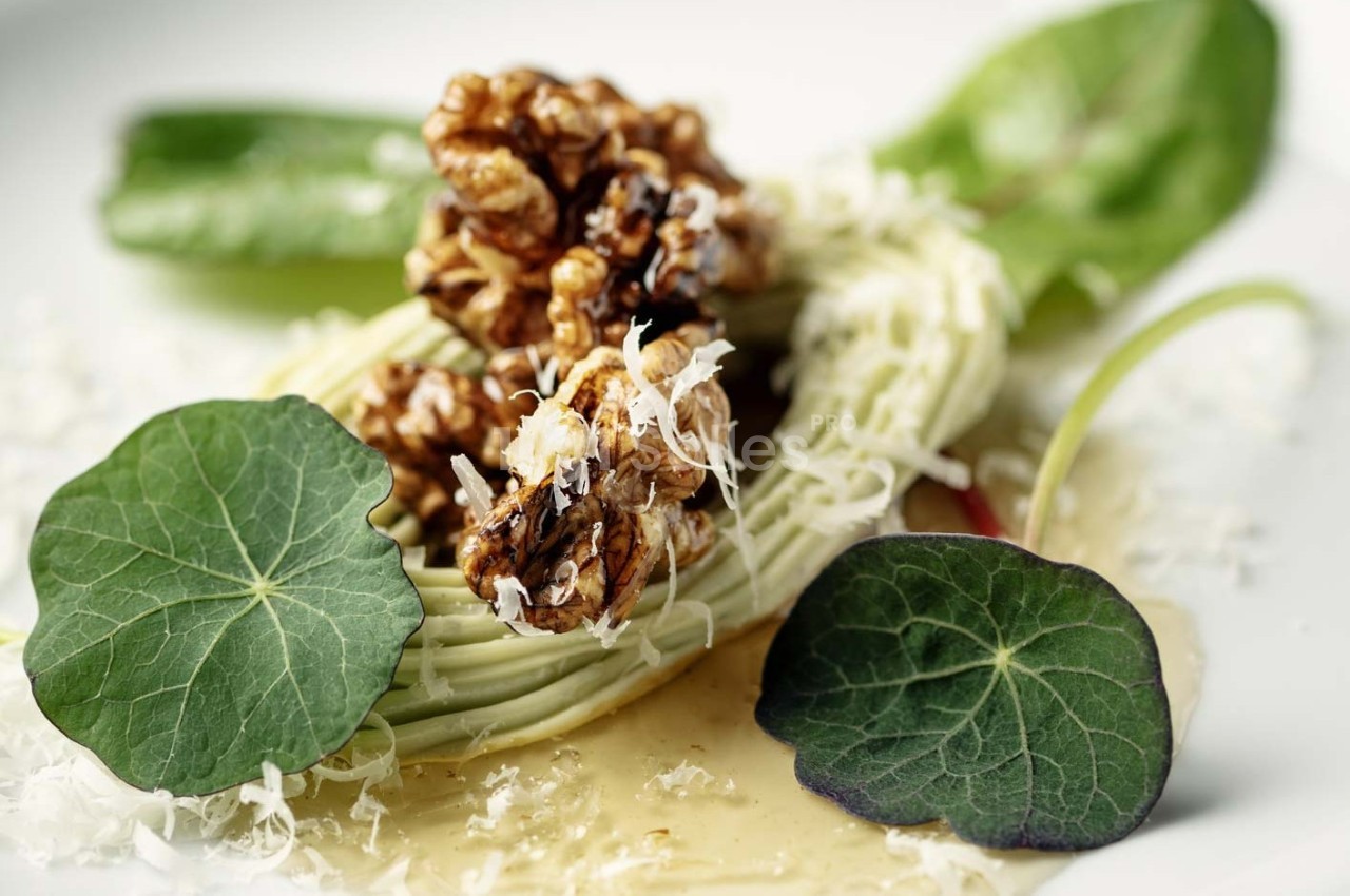 Assiette garnie de spaghettis de légumes, noix caramélisées, feuilles de capucine et copeaux de fromage.