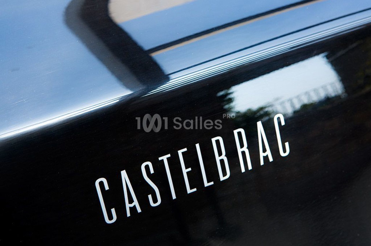 Texte ’Castelbrac’ inscrit sur une surface noire brillante, avec un reflet et un arrière-plan flou.