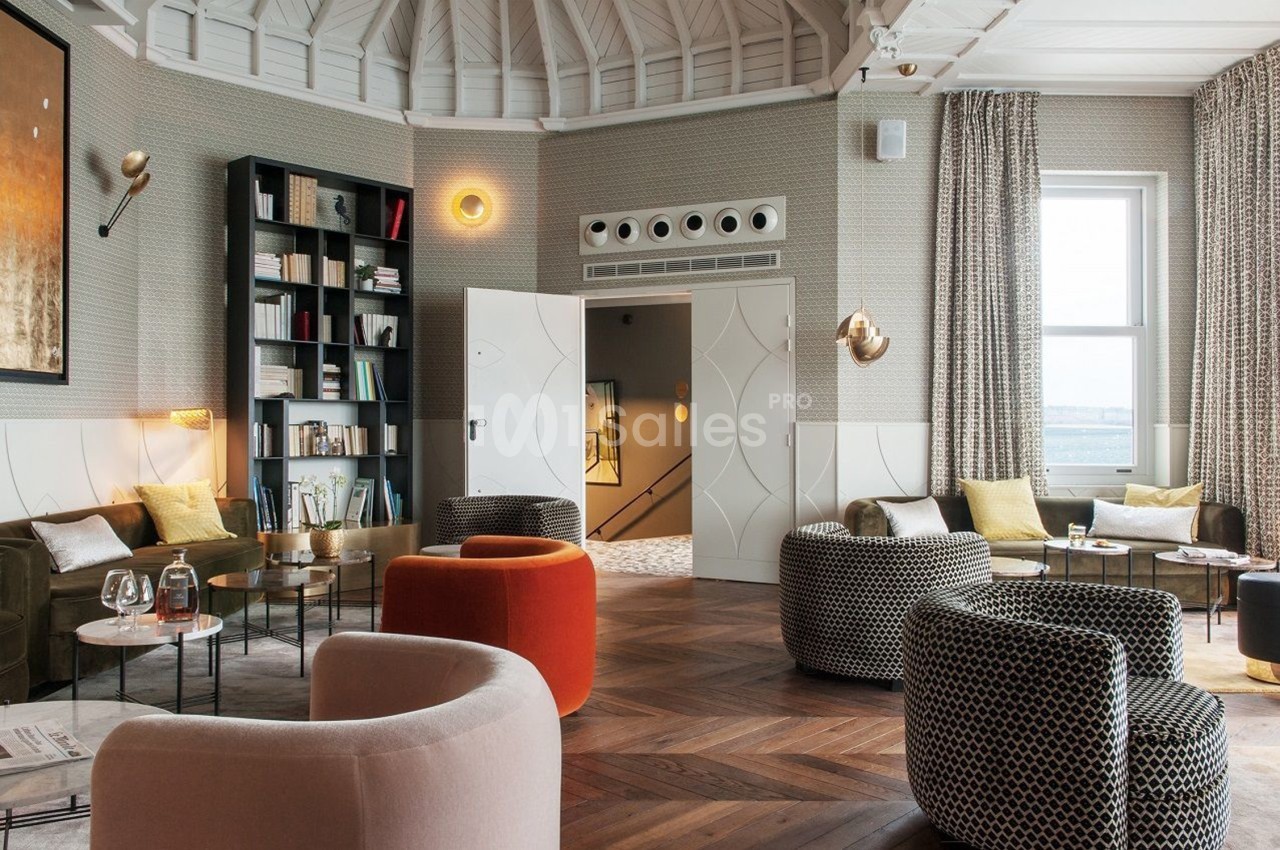Salon élégant avec fauteuils variés, bibliothèque, éclairage design et vue sur une fenêtre donnant sur l'extérieur.