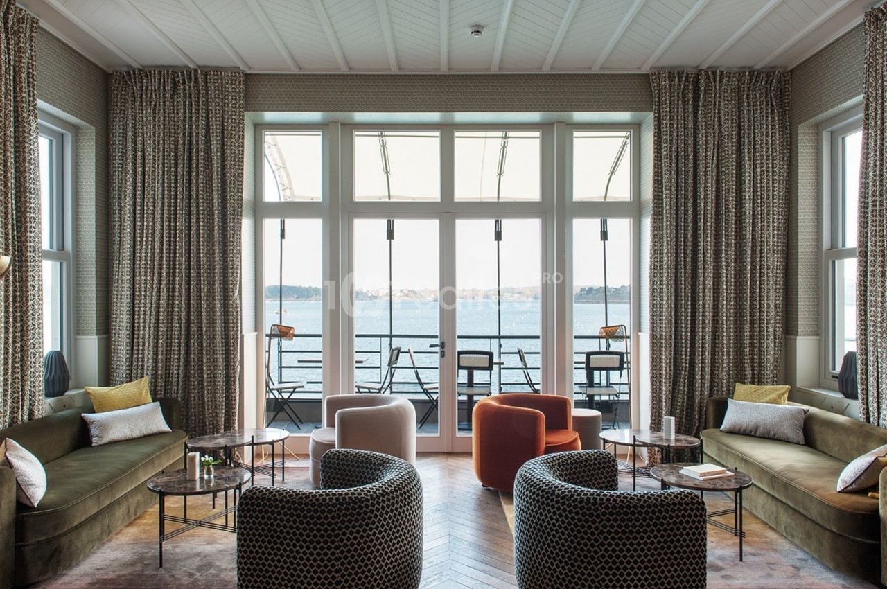 Salon lumineux avec grandes baies vitrées donnant sur une terrasse et une vue sur un plan d'eau.